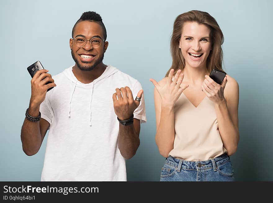 Surprised multiracial diverse people isolated on blue studio background hold smartphones look at camera amazed by unexpected news, multiethnic man and woman feel shocked using cellphones. Surprised multiracial diverse people isolated on blue studio background hold smartphones look at camera amazed by unexpected news, multiethnic man and woman feel shocked using cellphones