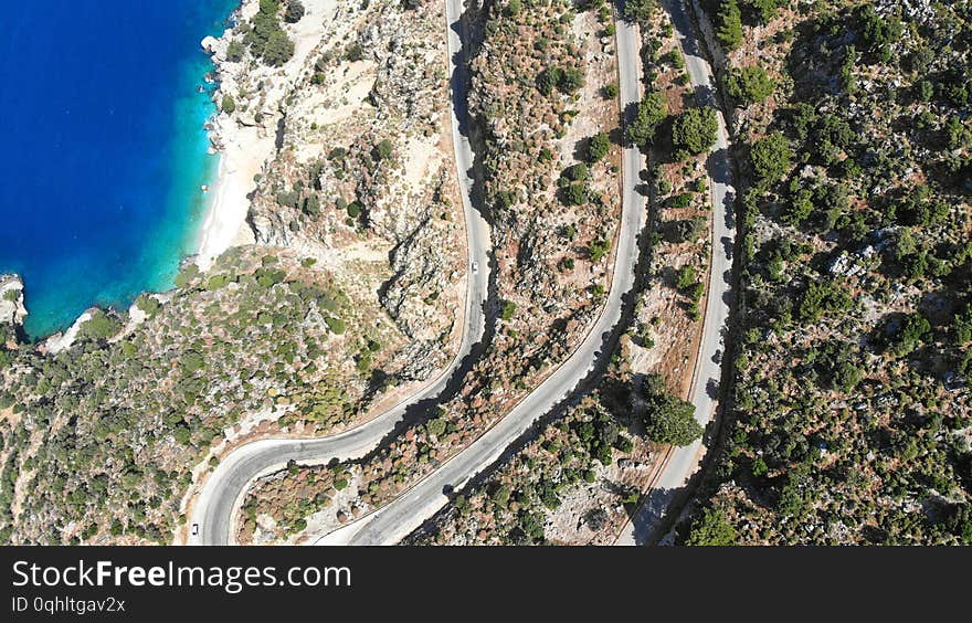 Aerial serpentine road. Traffic motion on a highway road in the mountains by the sea. Trip by car. Top view.