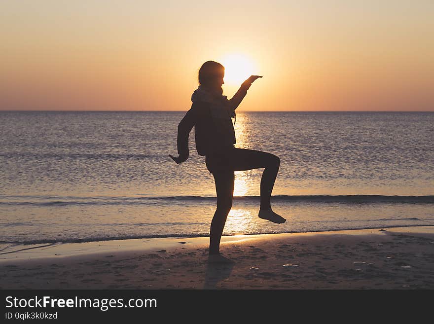 Sunset over the sea, woman is dancing on the beach