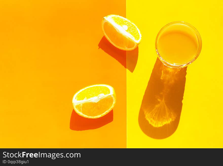 Glass of freshly squeezed citrus juice with pulp orange wedges on duotone yellow background. Harsh light hard shadows. Pop art 80s style aesthetics. Fitness summer vacation beach tropical concept