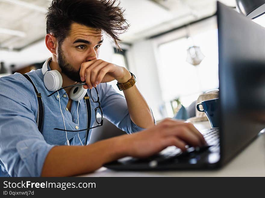 Young bearded businessman is sitting in front of computer, working. Freelancer, entrepreneur works at home.