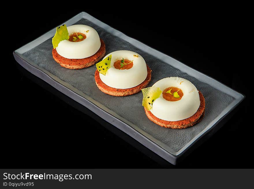 three cookies with white mousse cream, orande jam filling, and green decoration served on black background. three cookies with white mousse cream, orande jam filling, and green decoration served on black background