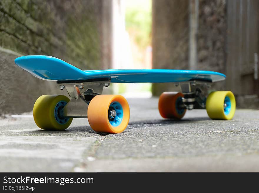 Blue plastic mini cruiser penny board or skate board with yellow and orange wheels on concrete tiles in an alley with light at the end. Low perspective, no people. Blue plastic mini cruiser penny board or skate board with yellow and orange wheels on concrete tiles in an alley with light at the end. Low perspective, no people.