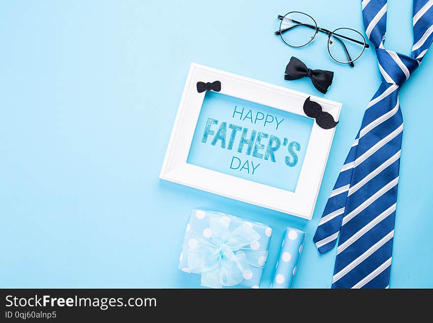 Happy fathers day concept. Top view of blue tie, beautiful gift box, white picture frame with Happy father`s day text on bright blue pastel background. Flat lay.