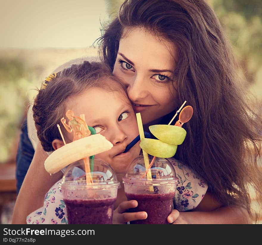 Happy kid girl and funny emotional mother drinking berries smoothie juice together in street summer outdoor cafe. Closeup toned portrait