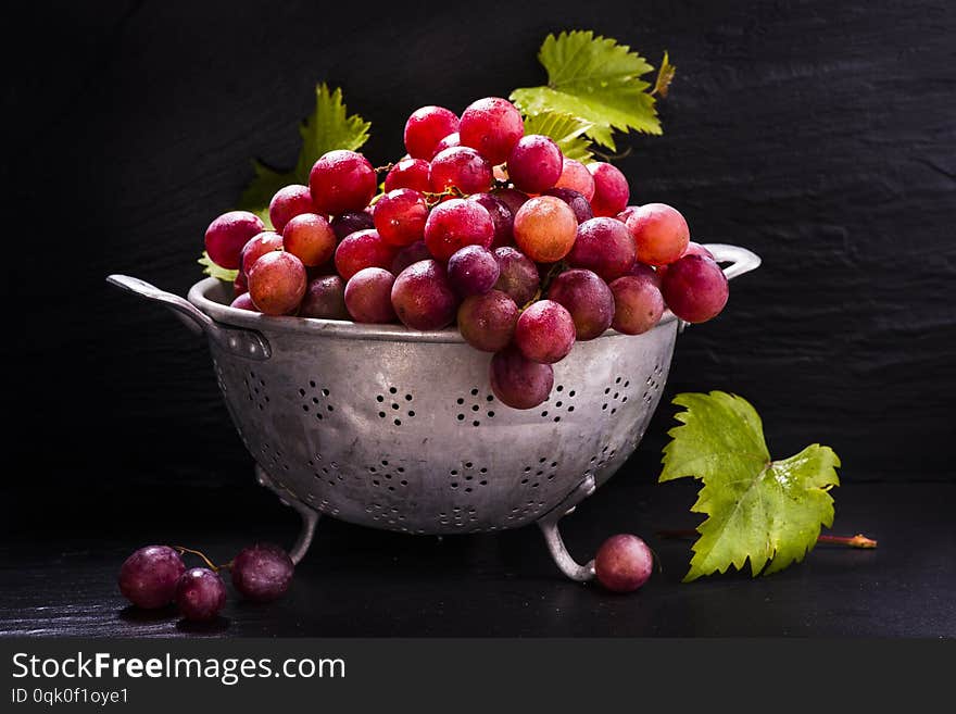 In colander vintage red table grapes with leaves .still life. In colander vintage red table grapes with leaves .still life