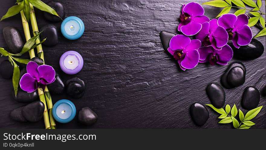 Spa.Group of black stones with purple orchid flowers, bamboo leaves and scented candles on a dark background. Spa.Group of black stones with purple orchid flowers, bamboo leaves and scented candles on a dark background