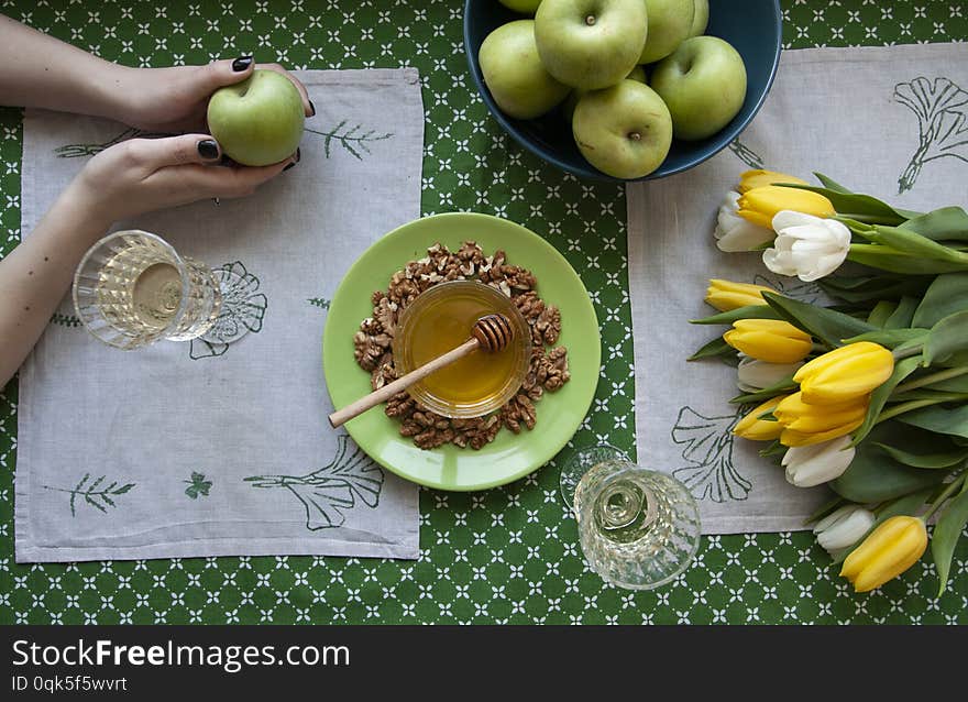 A gourmet lunch for two: fresh fruits, a bowl with honey with walnuts and two glasses wine; a bouquet of with tulips on a green tablecloth. A gourmet lunch for two: fresh fruits, a bowl with honey with walnuts and two glasses wine; a bouquet of with tulips on a green tablecloth