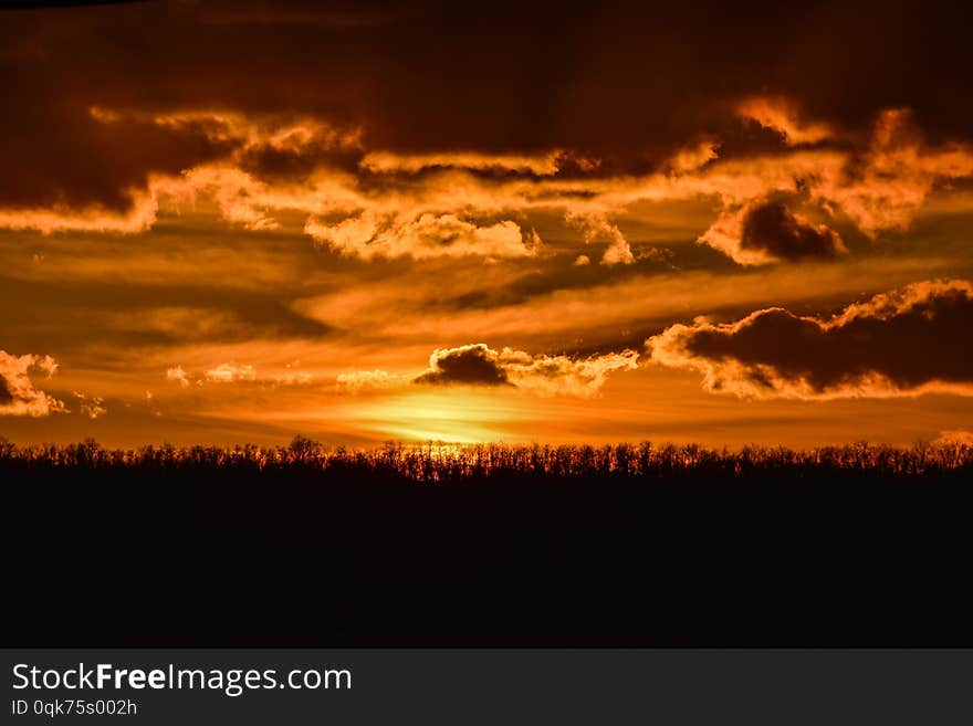 Dramatic cloudy orange sunset in the countryside over a line of trees. Dramatic cloudy orange sunset in the countryside over a line of trees