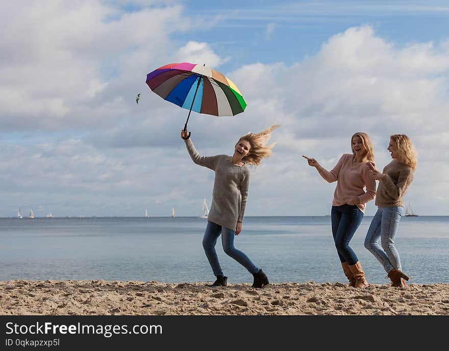 Female jumping with colorful umbrella her two friends are making fun of her laughing and looking. Female jumping with colorful umbrella her two friends are making fun of her laughing and looking