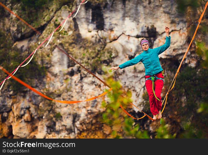 A woman is walking along a stretched sling. Highline in the mountains. Woman catches balance. Performance of a tightrope walker in nature. Highliner on the background of thunderclouds. Fall athlete