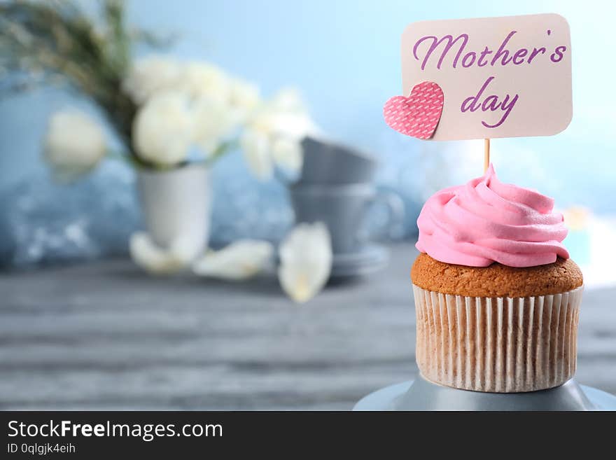 Tasty cupcake and topper pick with words MOTHER S DAY on table