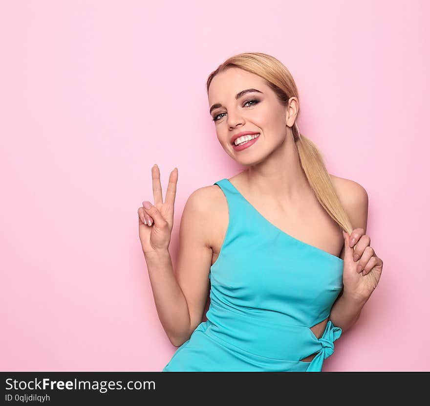 Beautiful young woman showing victory gesture on color background