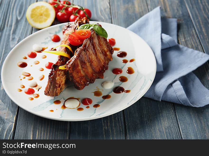 Plate with delicious grilled ribs and sauces on table