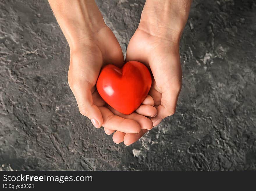 Hands of woman with red heart on dark textured background