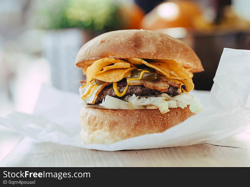 Fresh close-up of designer homemade burger with cutlet, bacon, chips and mustard sauce in craft paper on a wooden table