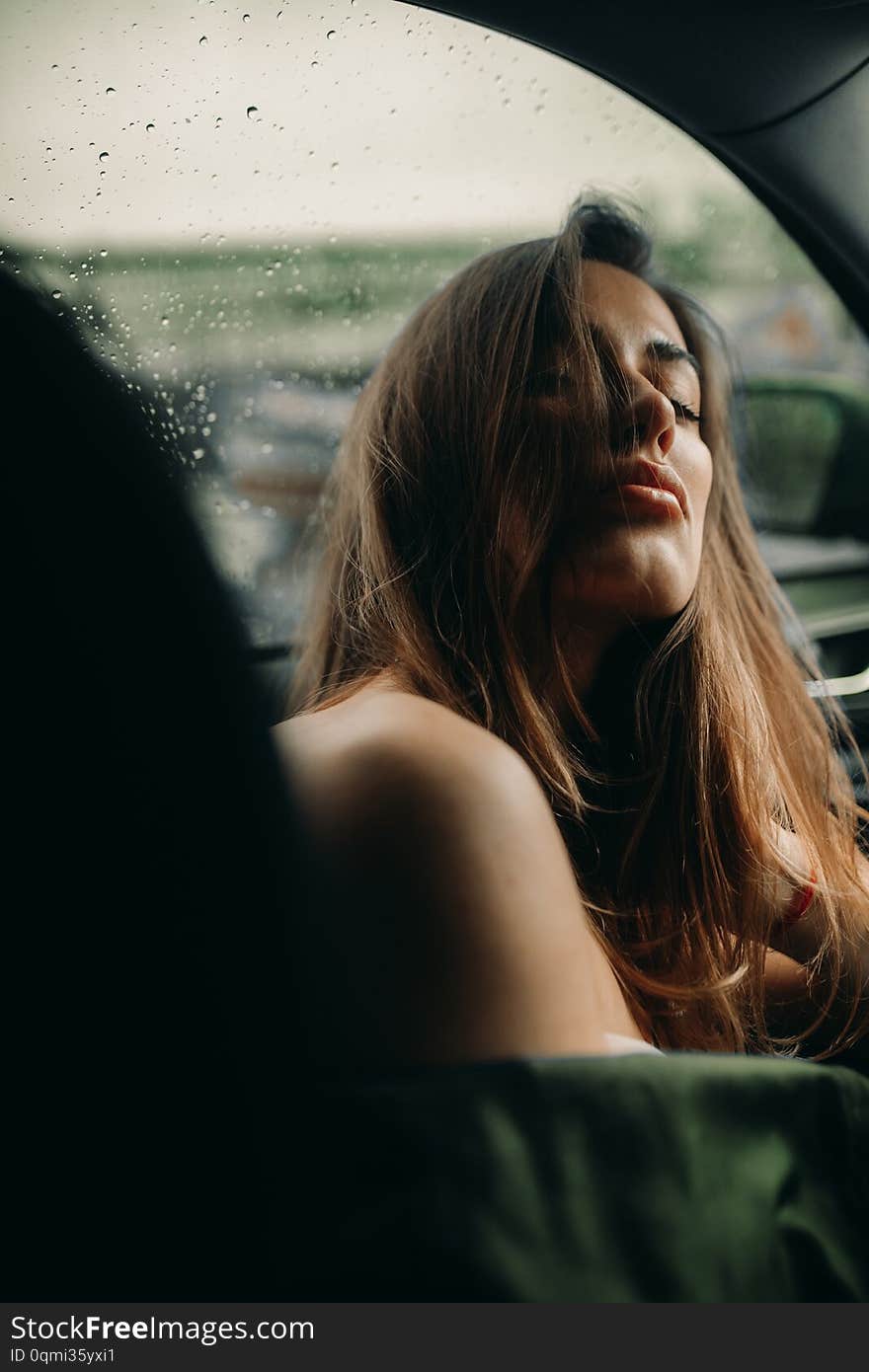 A Young Woman Sits Inside A Car Against The Background Of Raindrops