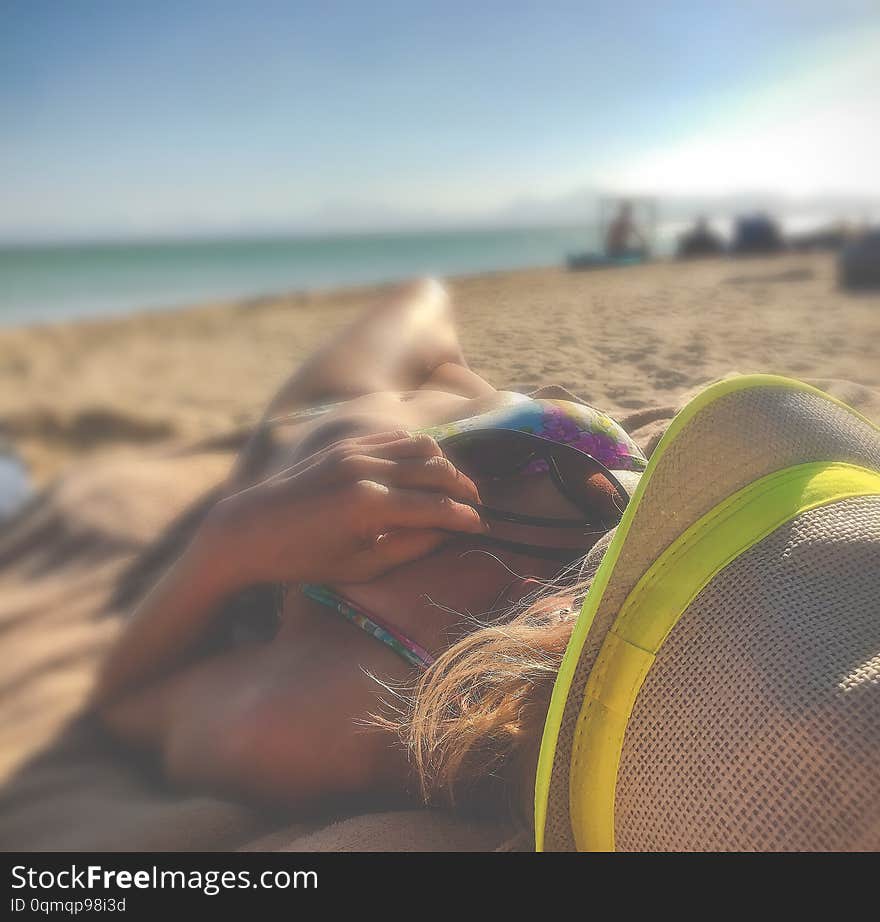 Beautiful tanned figure young girl lies on the beach in yellow hat from overheating sun