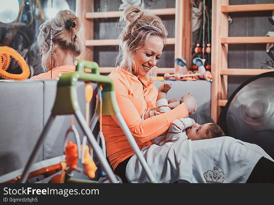 Cheerful happy mom is plaing with her pretty baby at pediatrician cabinet full of special treatment equipment. Cheerful happy mom is plaing with her pretty baby at pediatrician cabinet full of special treatment equipment.