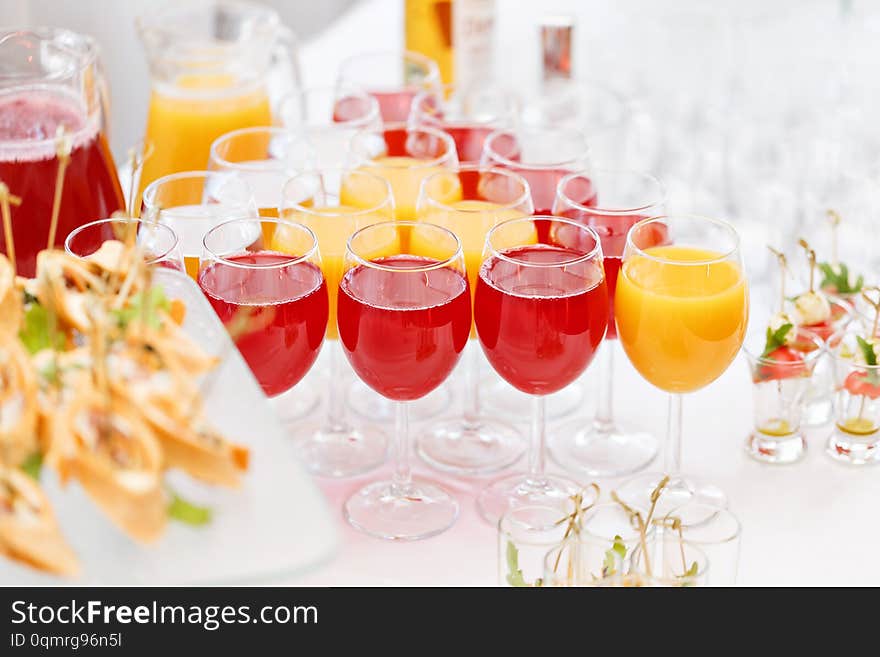 Table top full of glasse Glasses without alcohol drinks, orange juice, water and berry juice. s with canapes and antipasti in the background. Table top full of glasse Glasses without alcohol drinks, orange juice, water and berry juice. s with canapes and antipasti in the background