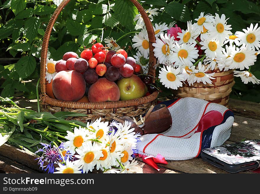 Juicy black grapes and apples, pears and peaches in a basket in the garden on an old wooden table, glasses and a cap, a smartphone surrounded by spring flowers with drops close-up, selective focus. Gathering in the country tasty, dietary and healthy food for a healthy lifestyle