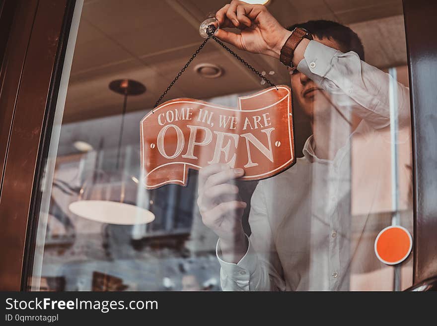 Man in white shirt is putting nameplate about opening at his own shop. Man in white shirt is putting nameplate about opening at his own shop.