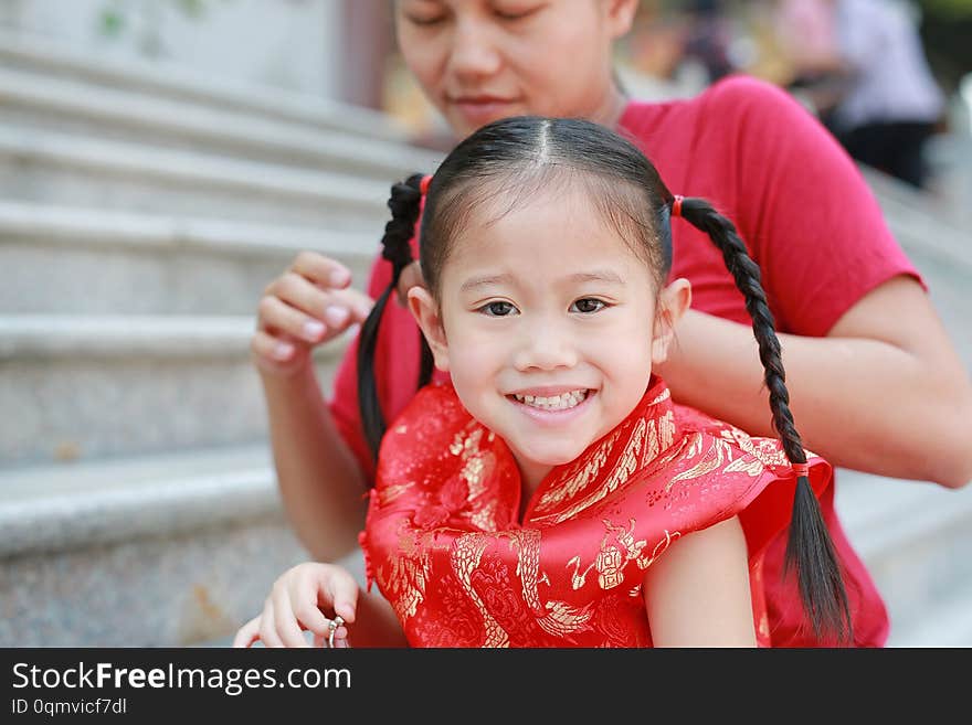 Portrait of Mother tying her daughter`s hair. Two tied ponytails hairs. Child girl looking at camera