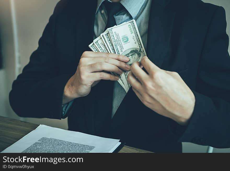 Businessman putting stack of money bills in his suit coat pocket