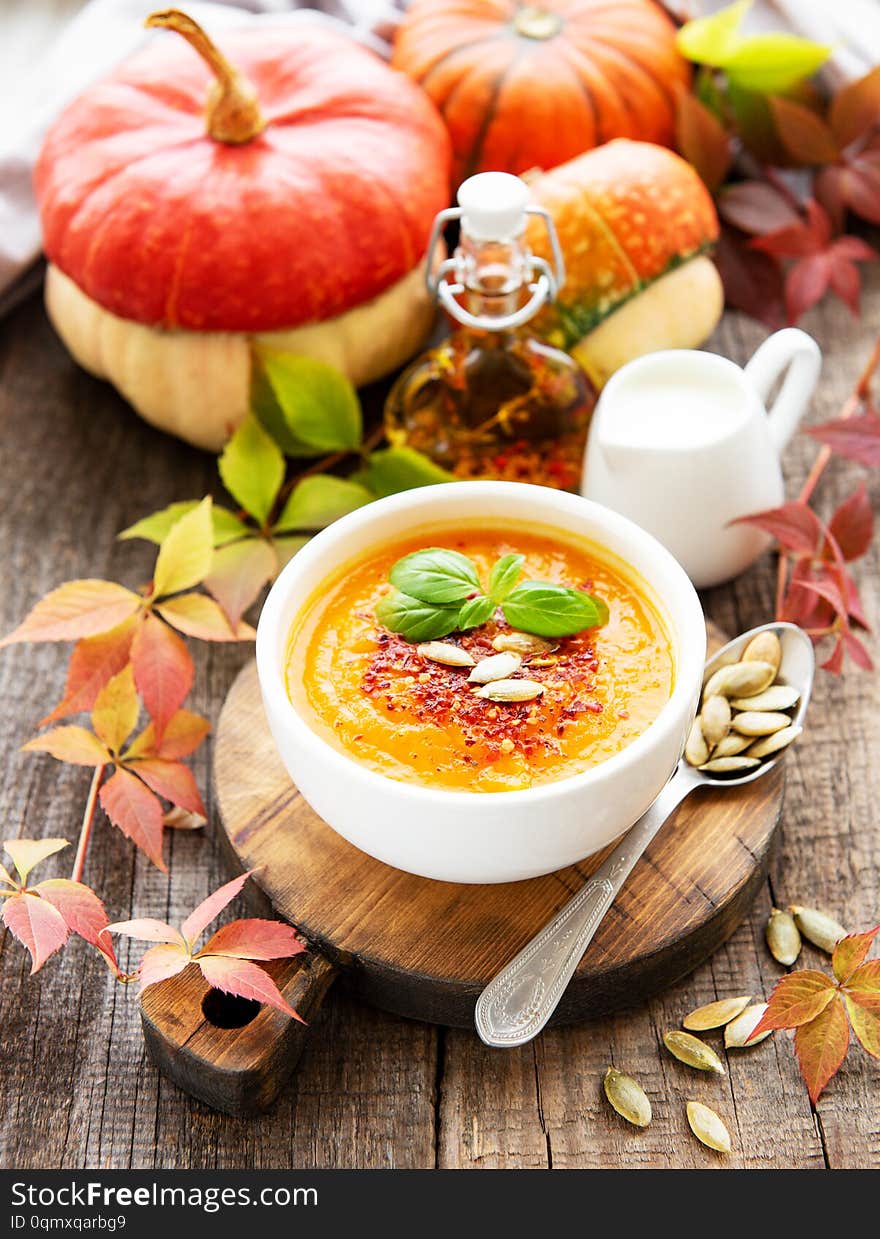 Bowl of pumpkin soup, fresh pumpkins and autumn leaves on rustic wooden background