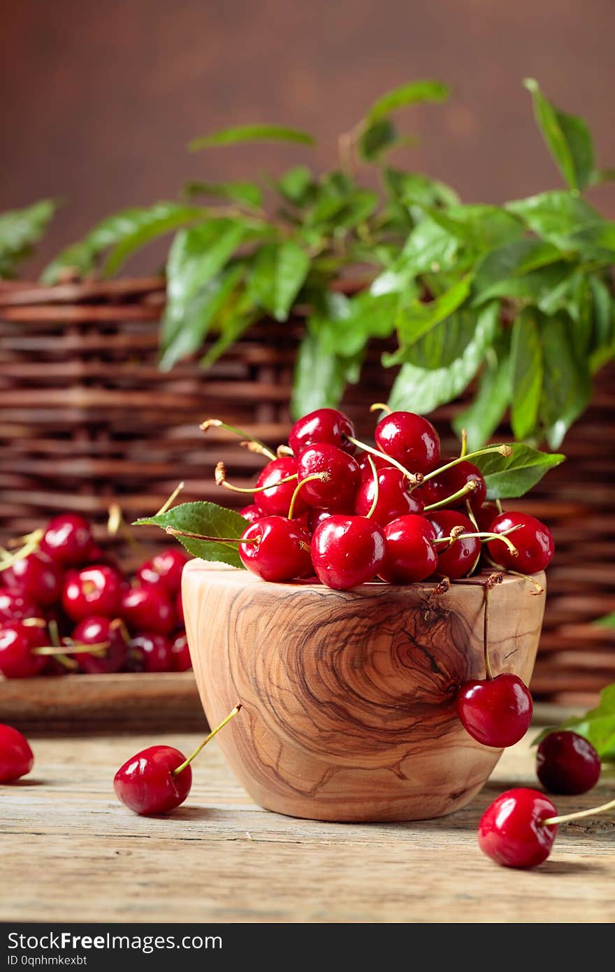 Red sweet cherry in a wooden bowl on a wooden table in garden. Wicker fence with green leaves in the background