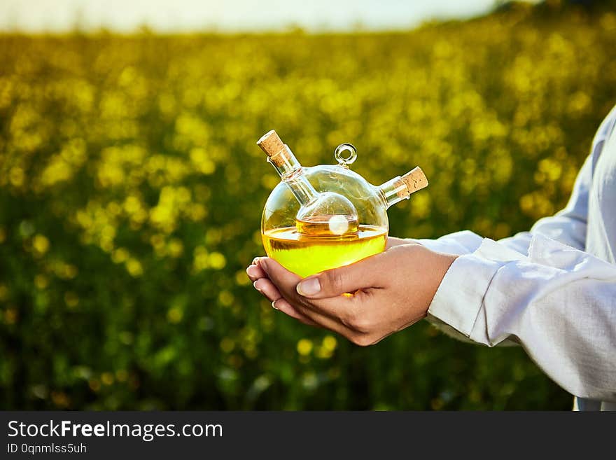 Rapeseed oil bottle in hand of an agronomist or biologist on background rape  field