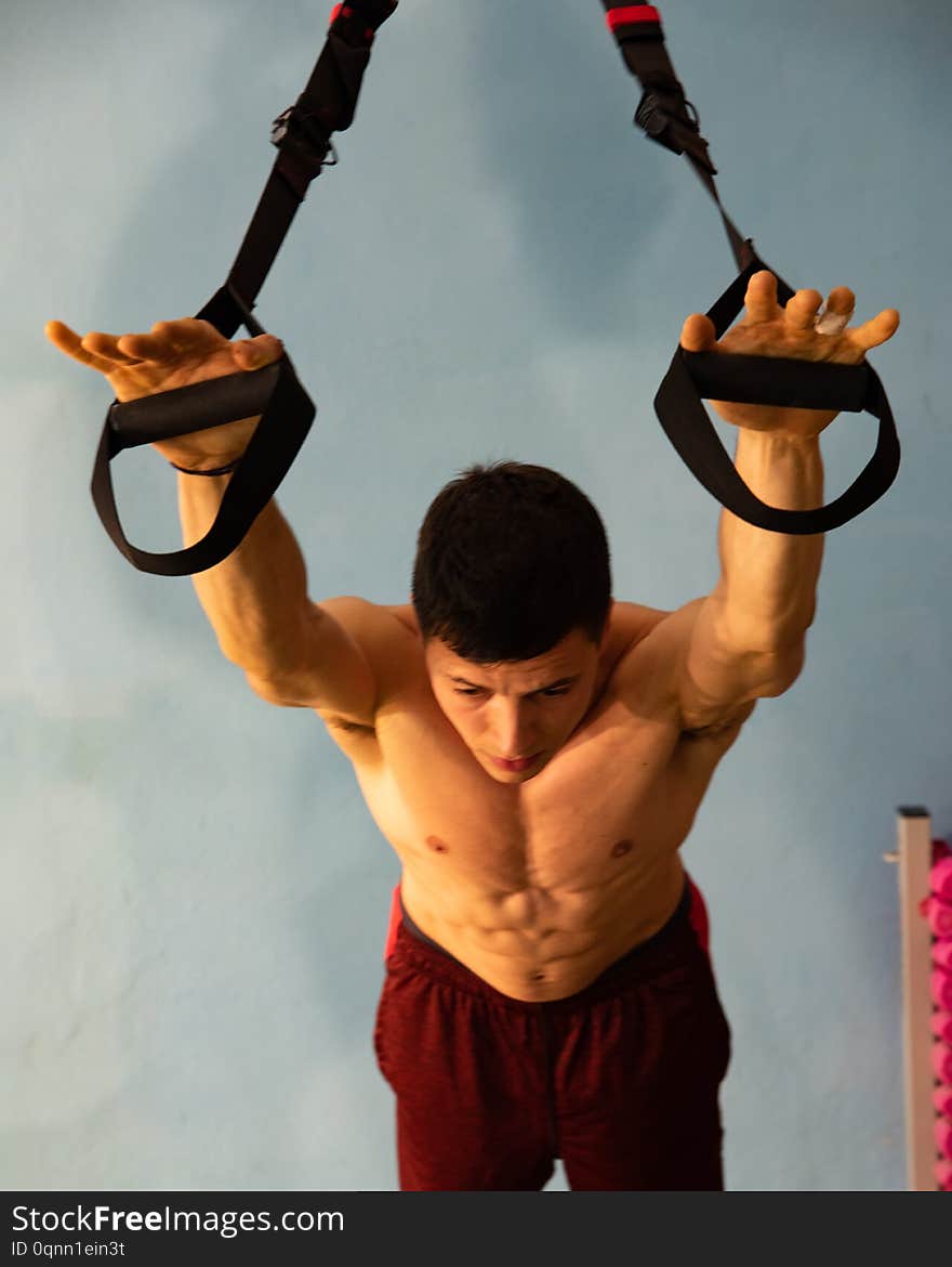 Young man does workout in the gym. Use TRX or `Suspension Training`