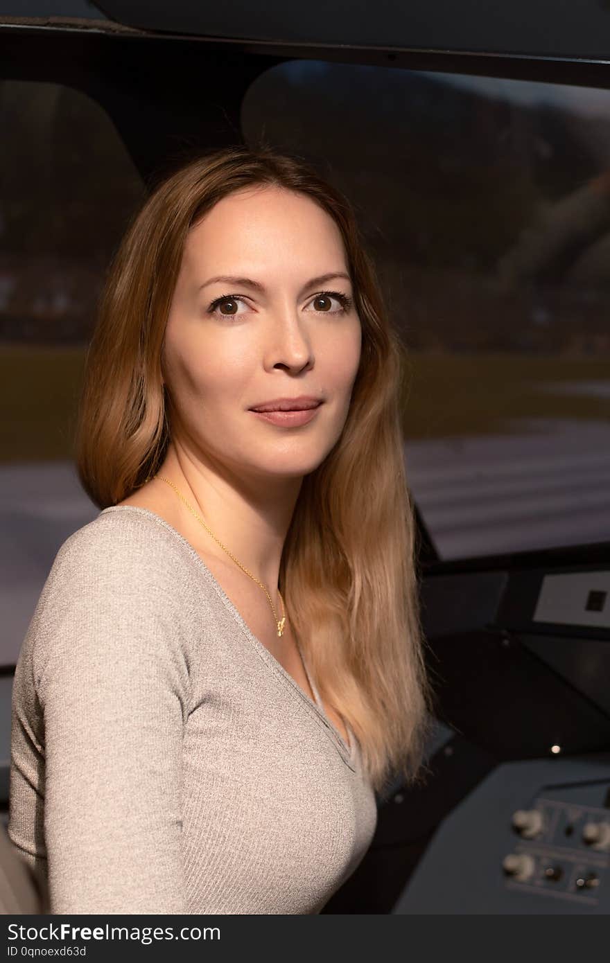 A young beautiful woman sits on the pilot`s seat in the seat at the helm and dashboard of an simulator airliner aircraft