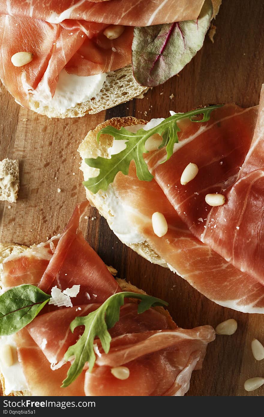 Traditional parma cured ham antipasto. Bruschetta set with Parma Ham and Parmesan Cheese. Small sandwiches with prosciutto, parmesan cheese, fresh arugula, olives and pine nuts on rustic wooden board