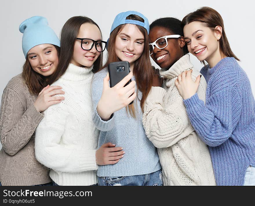 Lifestyle, friendship, tehnology and people concept: five different nation girls dressed in casual wear make selfie with a smartphone over white background