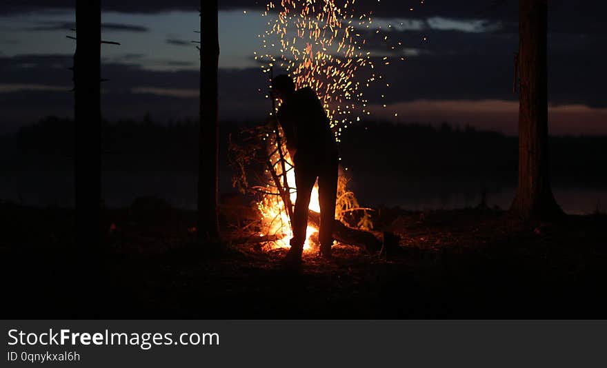 Silhouette of a man near the fire at night against the sky.