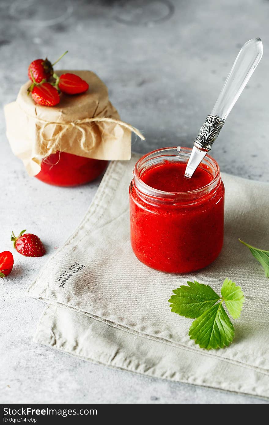 Homemade strawberry jam in glass jar on the wooden box on the gray background. Wild strawberry jam in swing-top jar on wood with strawberries in the back. Food photography. Seasonal cooking concept