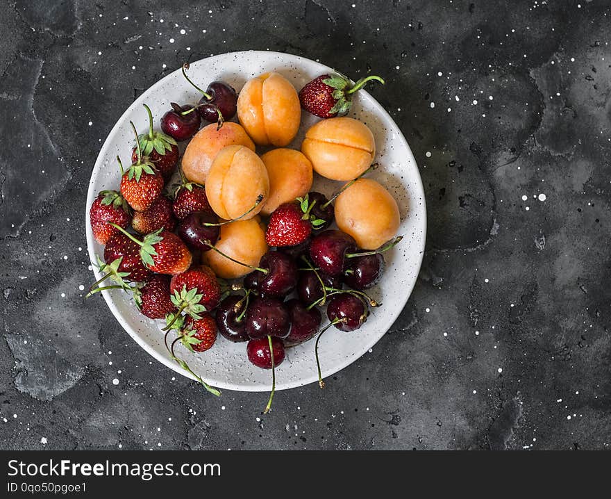 Fresh ripe fruit - apricots, cherries, strawberries on a dark background, top view