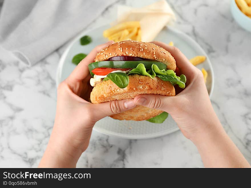 Woman holding tasty burger over plate at table, top view