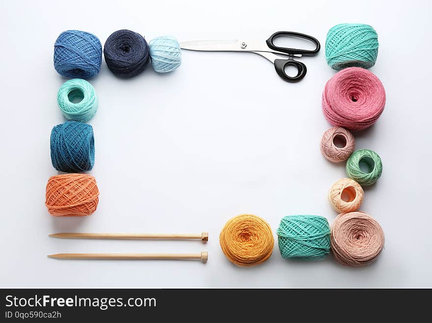 Frame made with clews of colorful knitting threads and accessories on white background, flat lay