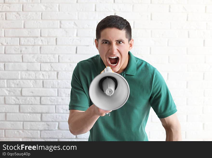 Portrait of young man using megaphone near brick wall