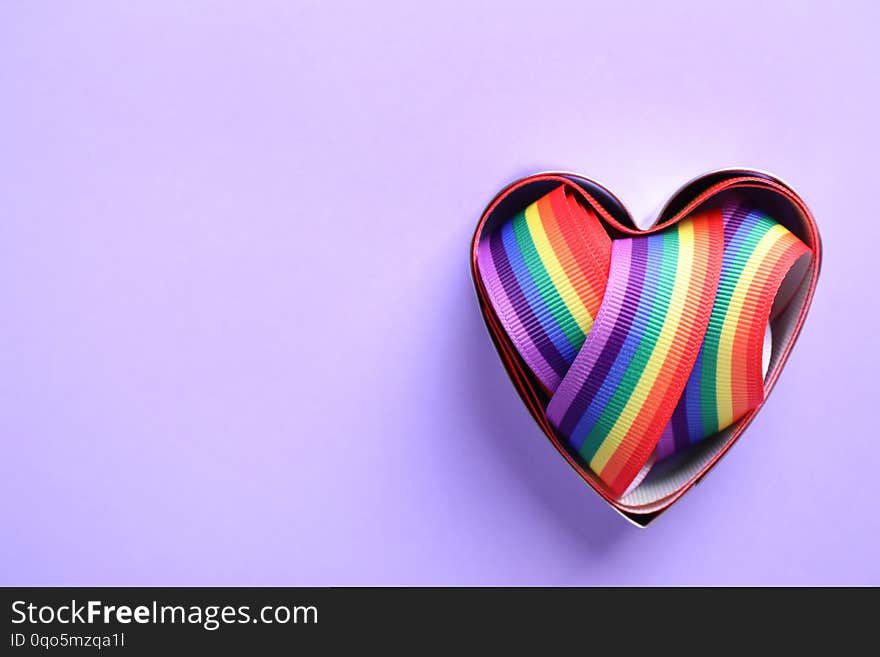 Heart shaped mold and bright rainbow ribbon on color background, top view. Symbol of gay community