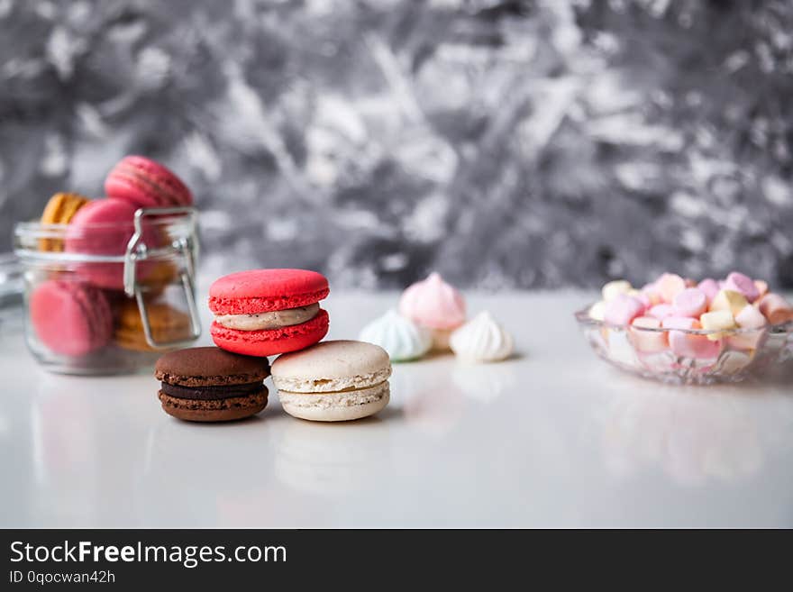 Colorful macaroons in a glass jar with marshmallows on the white table. Colorful macaroons in a glass jar with marshmallows on the white table