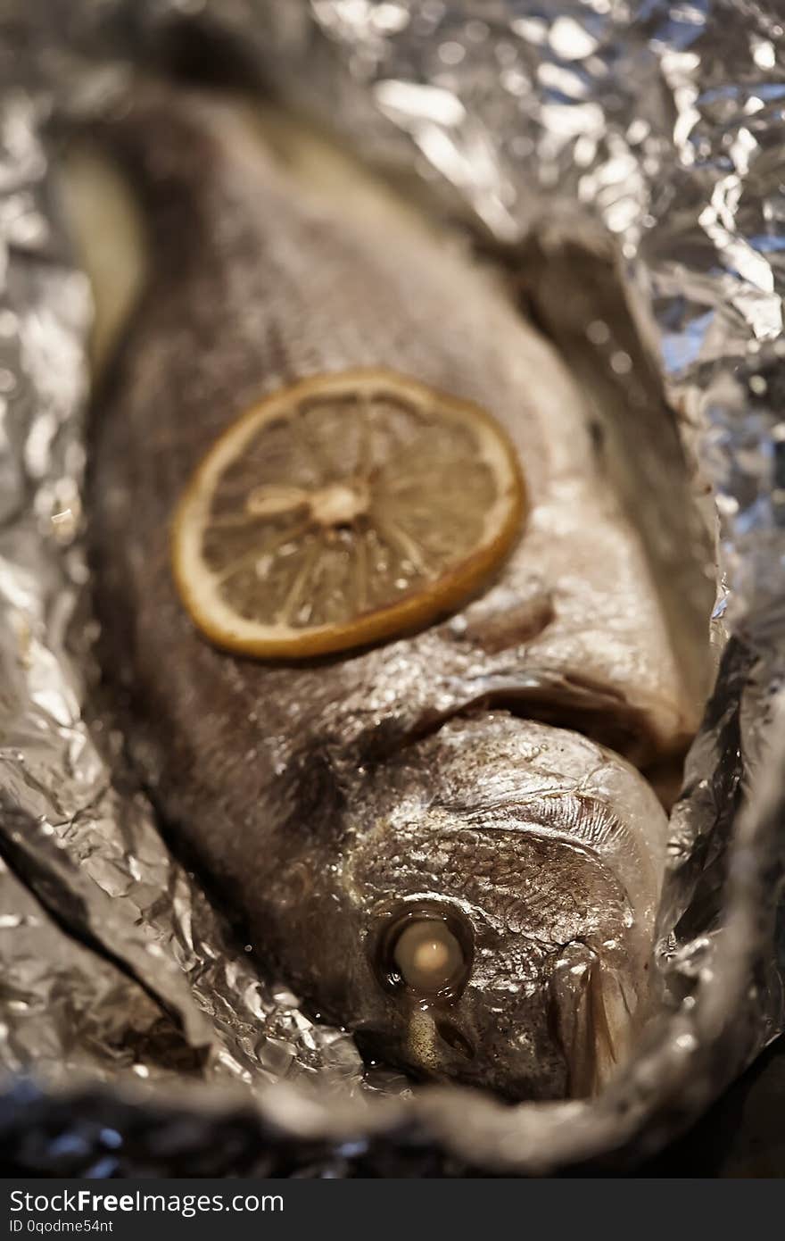 Baked sea bream fish is on a sheet of foil. On the fish is slice of lemon. Baked sea bream fish is on a sheet of foil. On the fish is slice of lemon