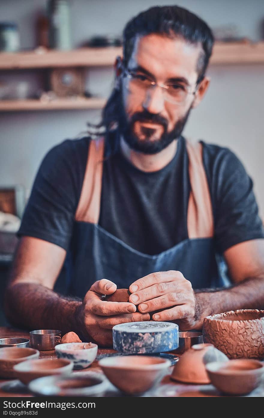 Diligent man in glasses at his pottery workshop is workig for new project.