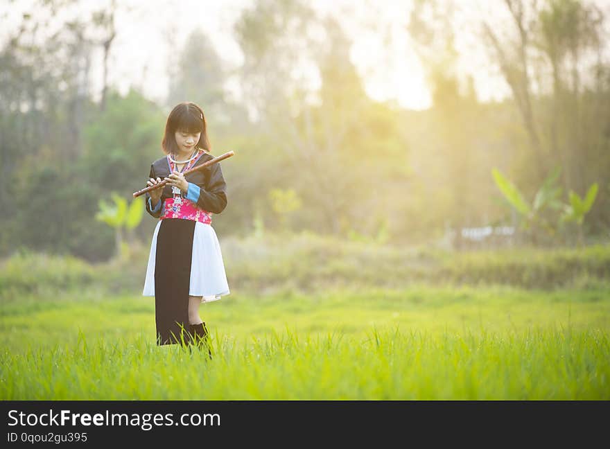 Tribe asian lady girl in custom dress hand hold flute with happy face walking in rice field in monsoon period.