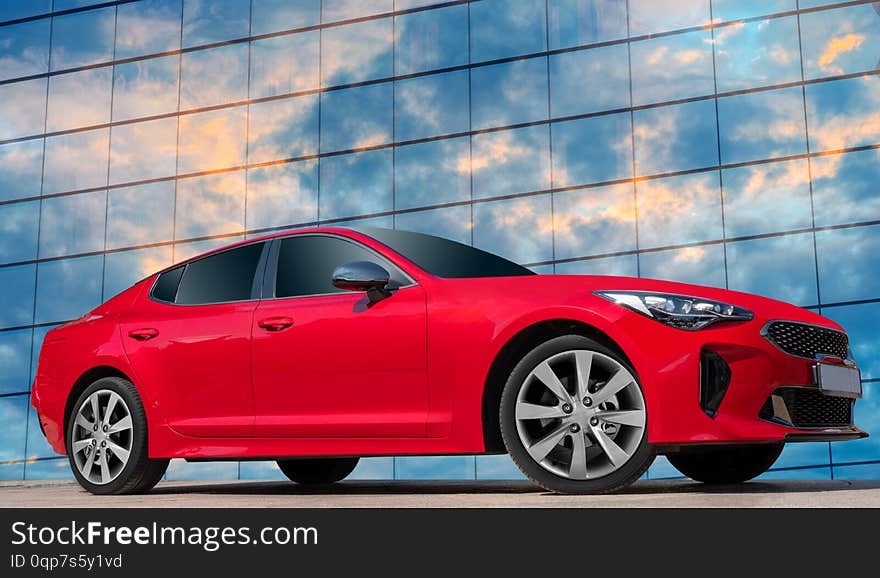 Red car on a glass building background. Reflections of the sky and clouds.