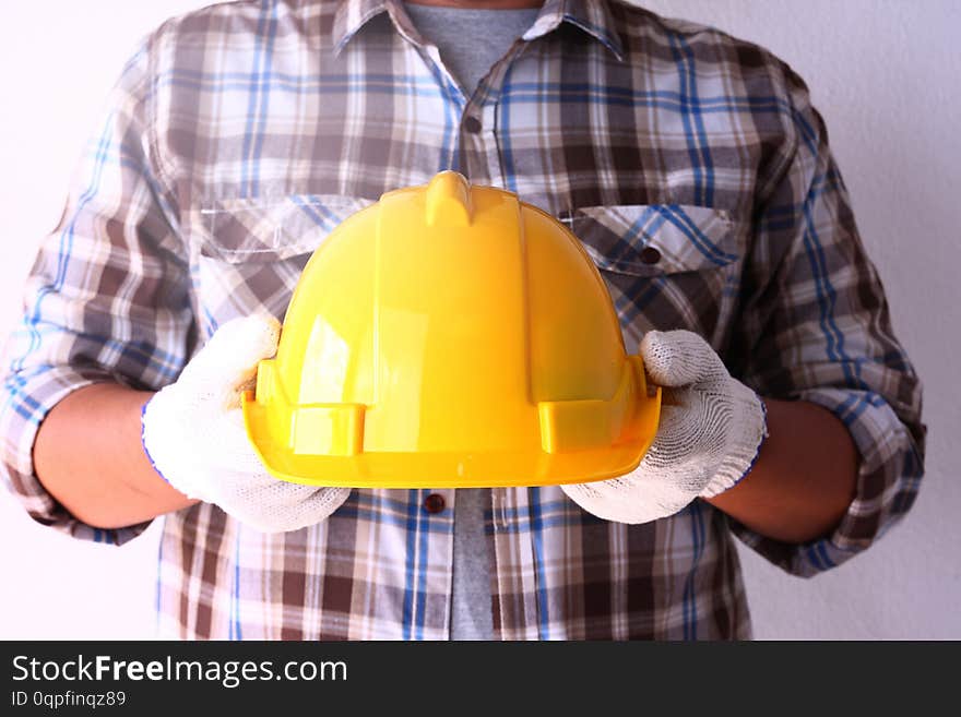 The construction worker wears white gloves, holding a yellow safety helmet for work safety. The construction worker wears white gloves, holding a yellow safety helmet for work safety