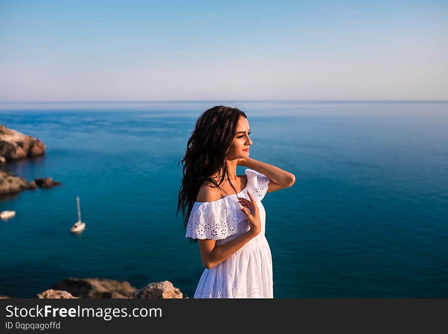 Young beautiful woman standing in white dress on the rock in the sea. Young beautiful woman standing in white dress on the rock in the sea.