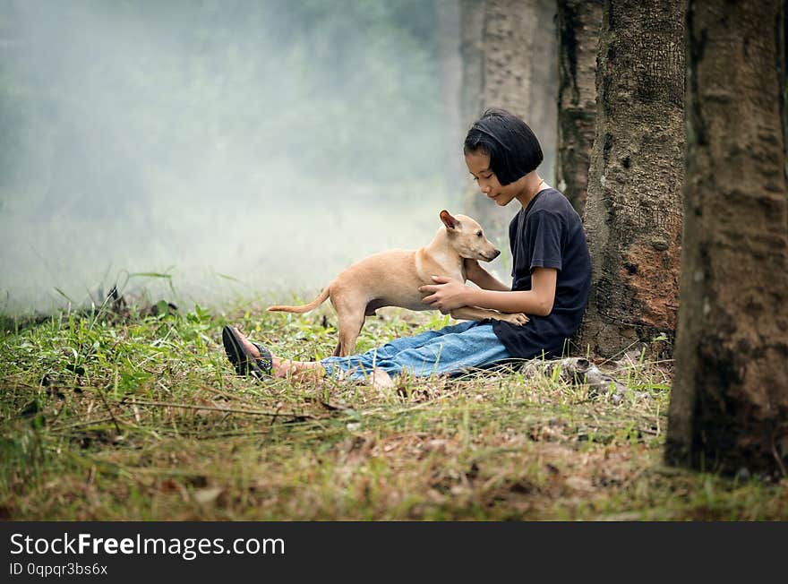 Little Asian girl sitting alone on green field under the tree with her dog, outdoor at countryside of Thailand ok